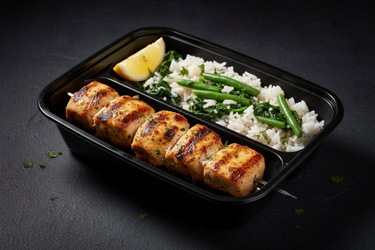 Greek chicken kabobs in a black meal prep container with rice, spinach and green beans
